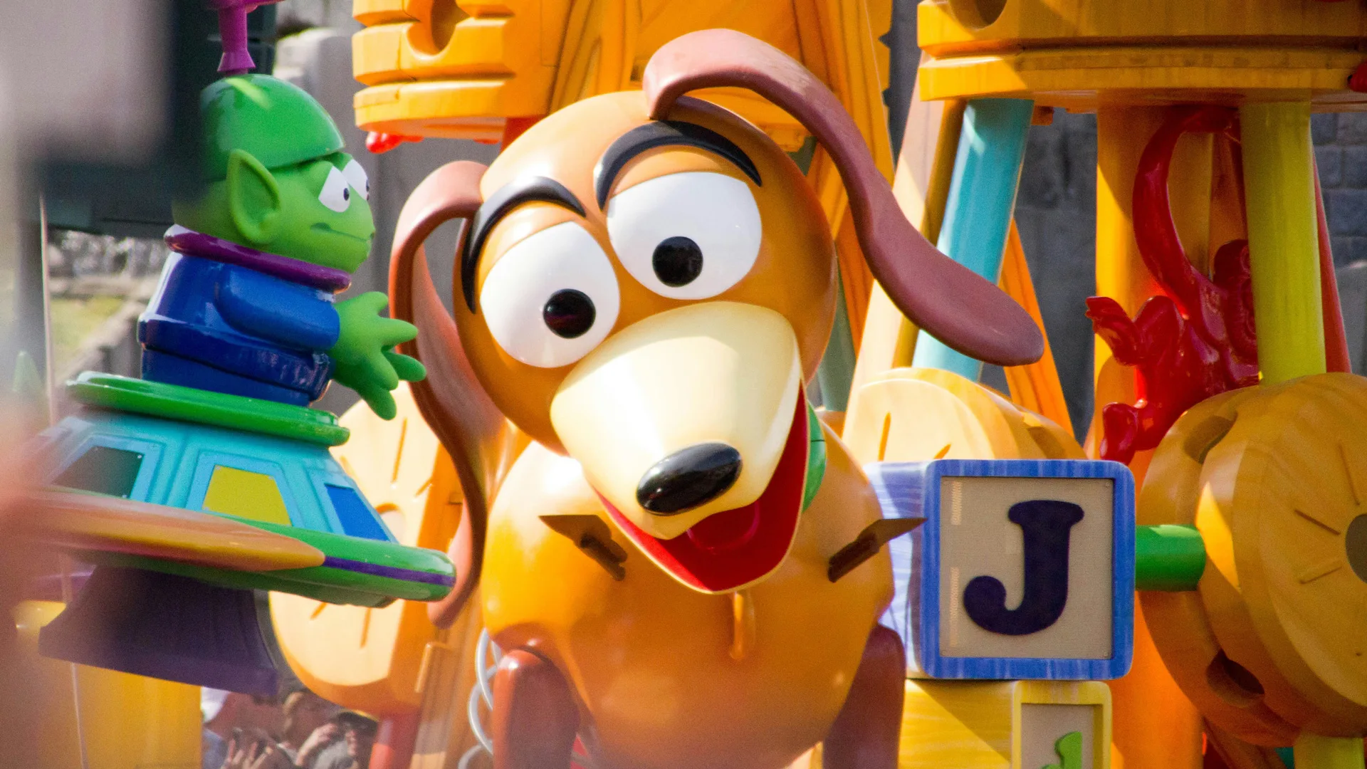 A photo of Slinky the dog from Toy Story looking down at something surrounded by toy alphabet letter blocks and the green alien next to him.