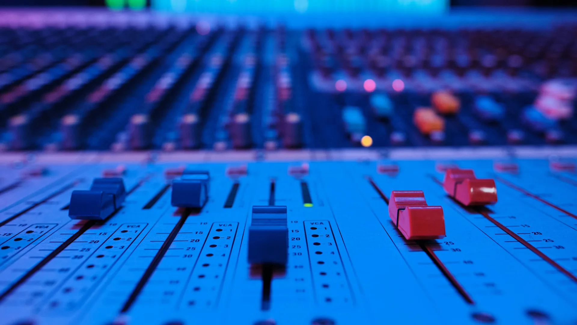 A photo of a sound recording board with sliding switches and knobs lit in blue.