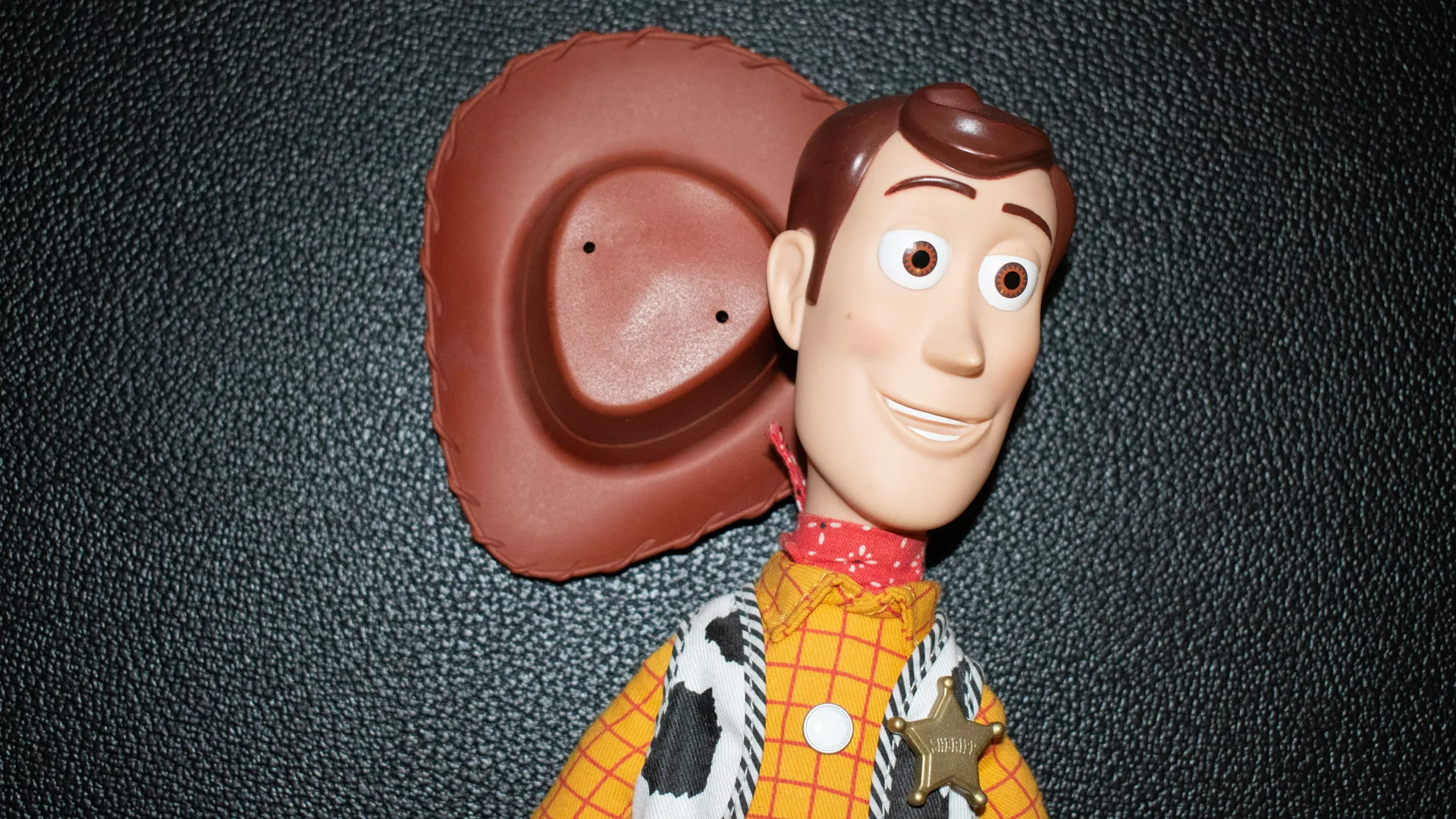 A photo of Woody from Toy Story lying against a dark grey floor with his hat next to his head.