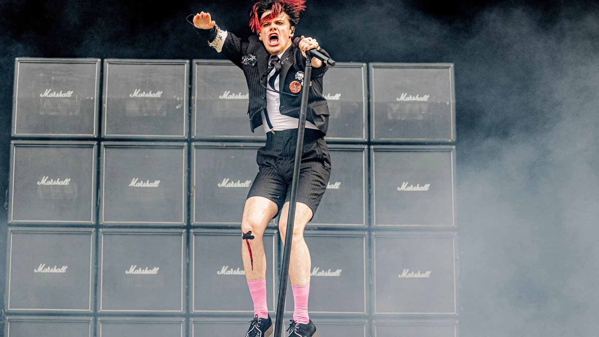 A photo of the singer Yungblud jumping mid air on stage holding the mic against a stack of Marshall amps.