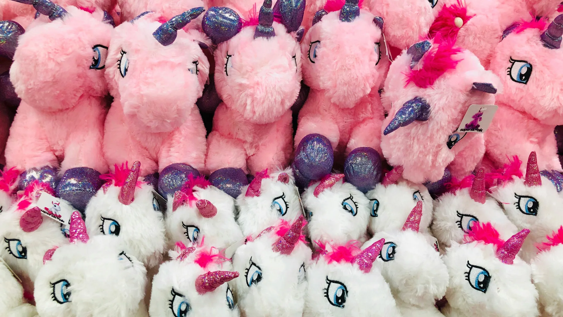 A photo of pink and white plush unicorns in a row piled up on top of eachother