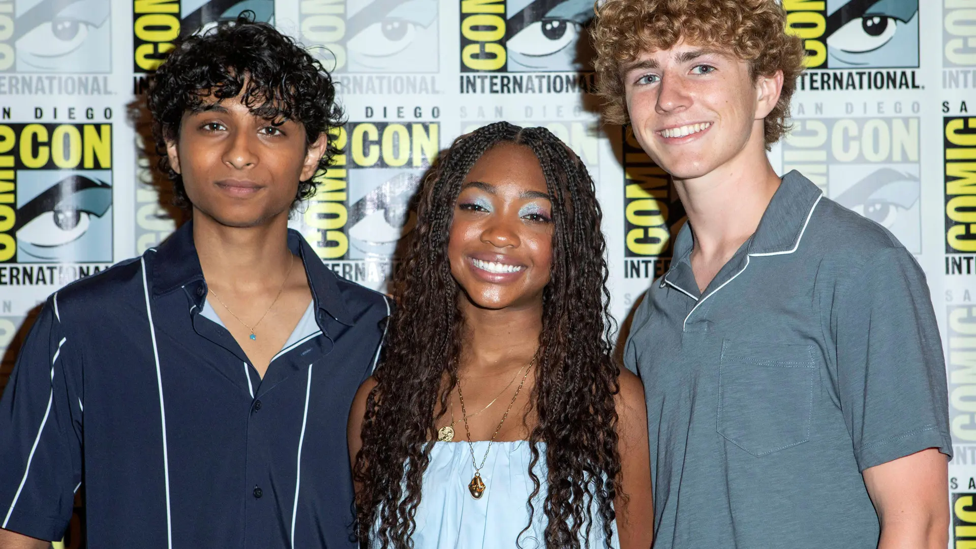 A photo of the three actors from Percy Jackson TV series stood in a line smiling against a COMIC CON branded background.