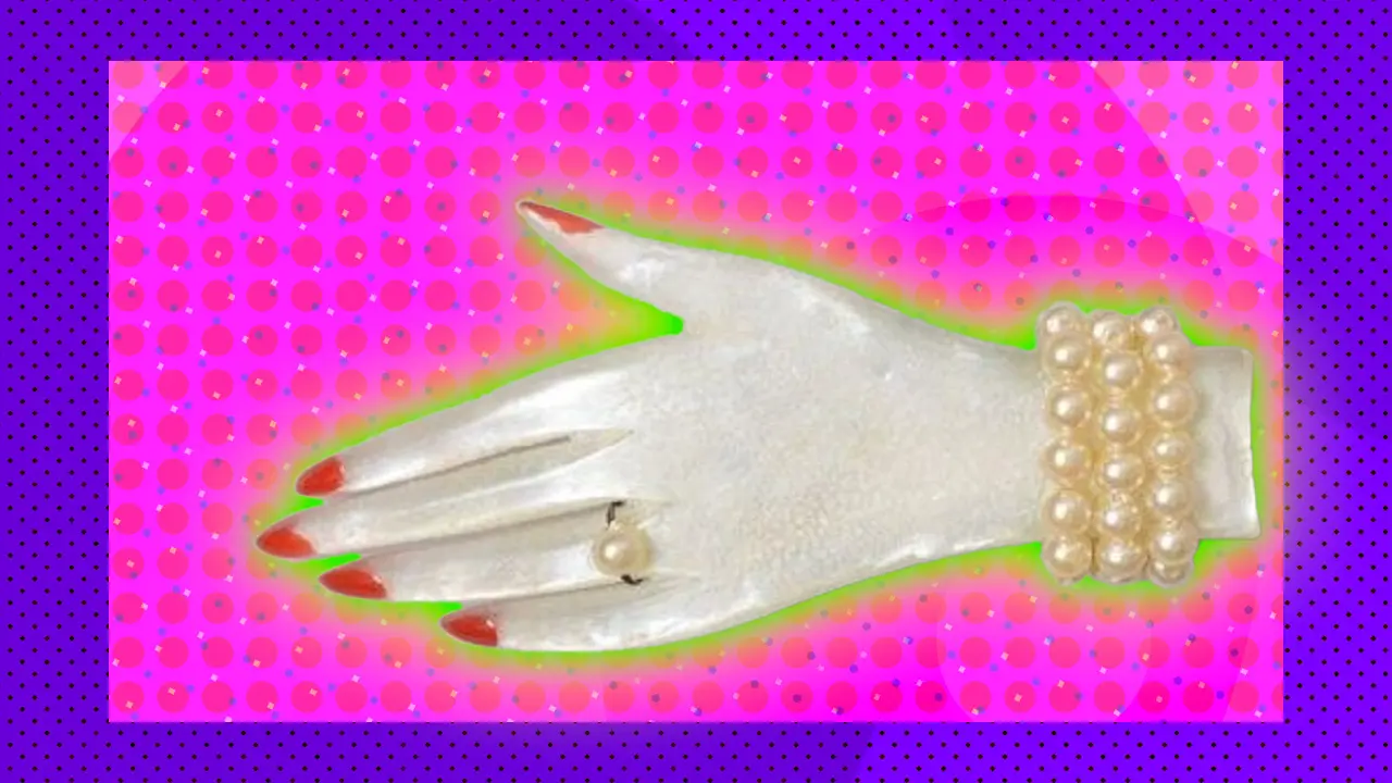 A photo of a pearl brooch in the shape of a hand with a little pearl bracelet and ruby fingernails set against a pink and purple background with a green halo.