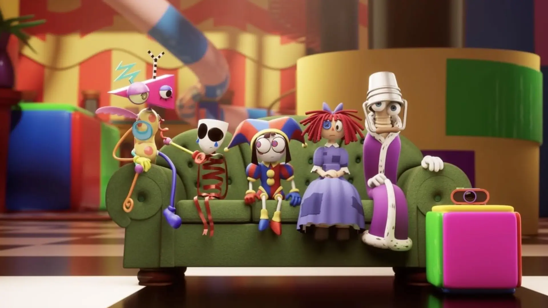 A still from The Amazing Digital Circus showing the characters sat on a giant green sofa in a room with colourful objects in the background.