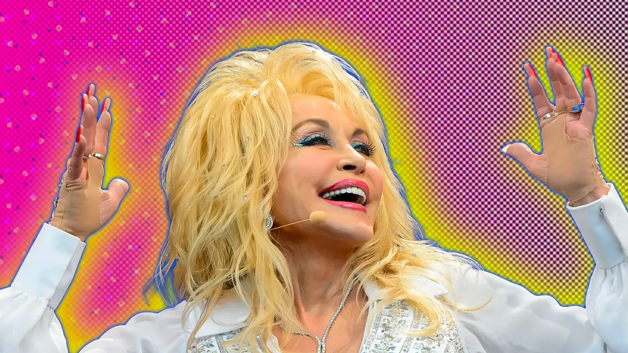A photo of Dolly Parton smiling up above her with her hands held up either side of her head in a white rhinestone top set against a pink background with a blue and yellow halo.