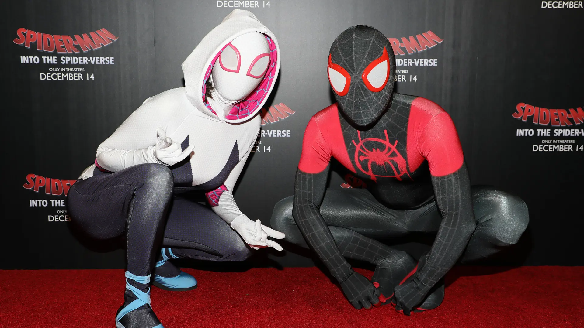 An image of two people dressed as Spider Gwen and Spider-Man at a premier of Into the Spiderverse with a red carpet beneath them and a billboard behind.