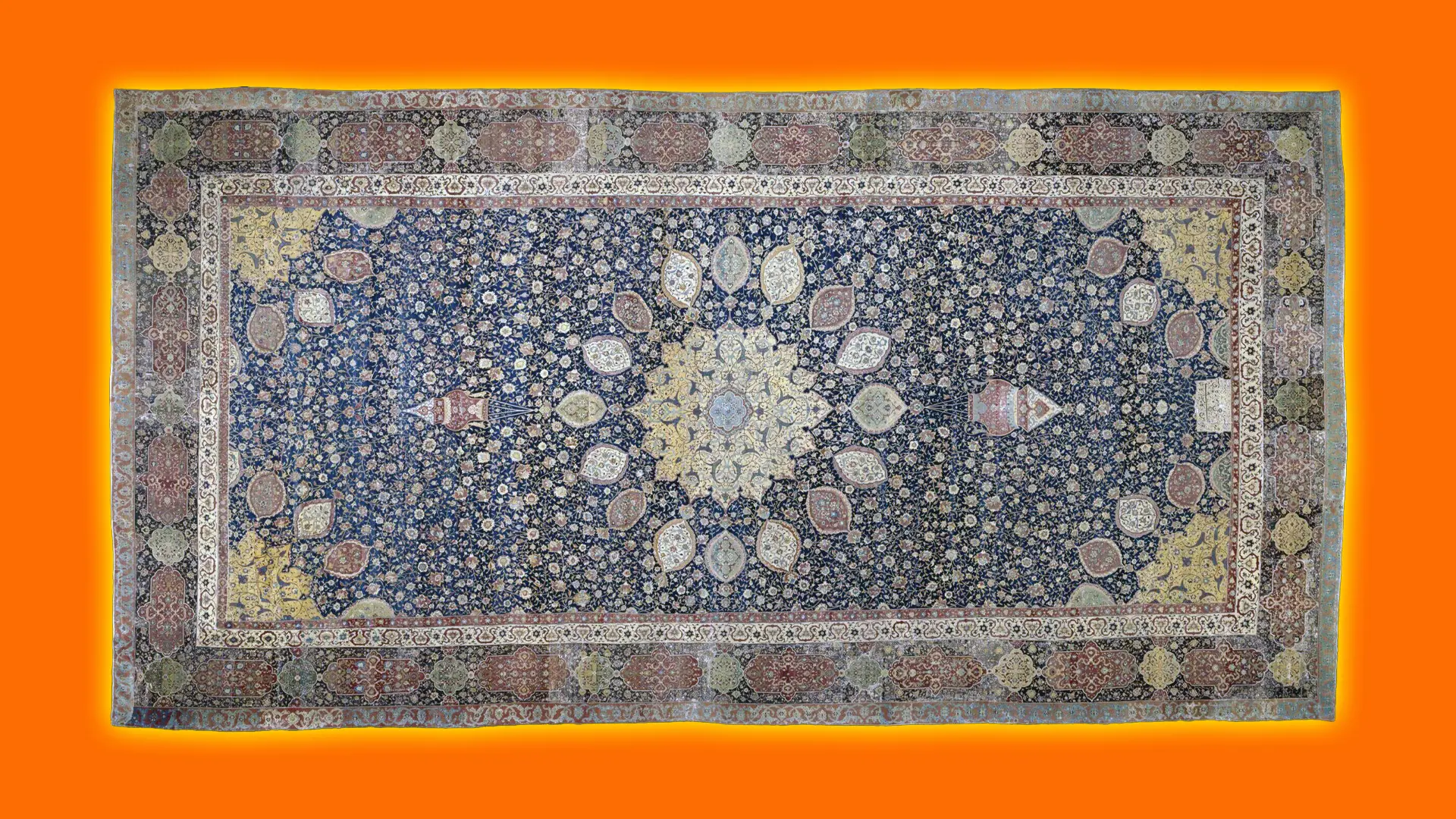 A photo of the Ardabil Carpet - a knotted wool carpet in colours of blues reds beige set against an orange background with a yellow halo.