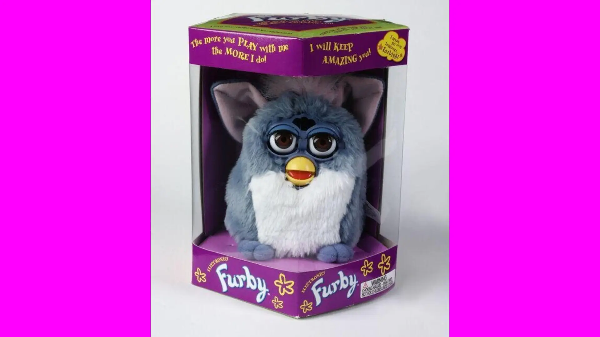 A photo of a Furby toy in it's original box against a white background with pink borders either side.
