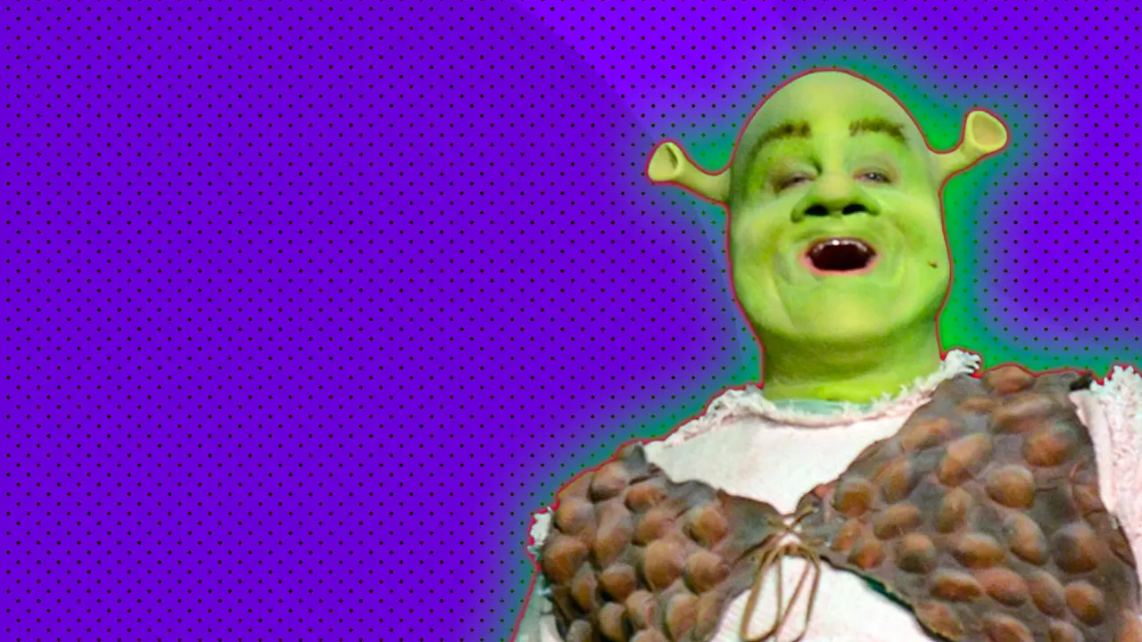 An image of a man playing Shrek with full green makeup and prosthetics and a white shirt with brown waistcoat set against a purple dotted background with a red and green halo.