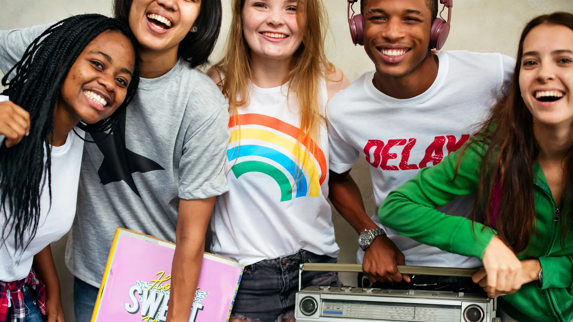 A photo of a group of friends lined up smiling at the viewer - one is holding a retro stereo.