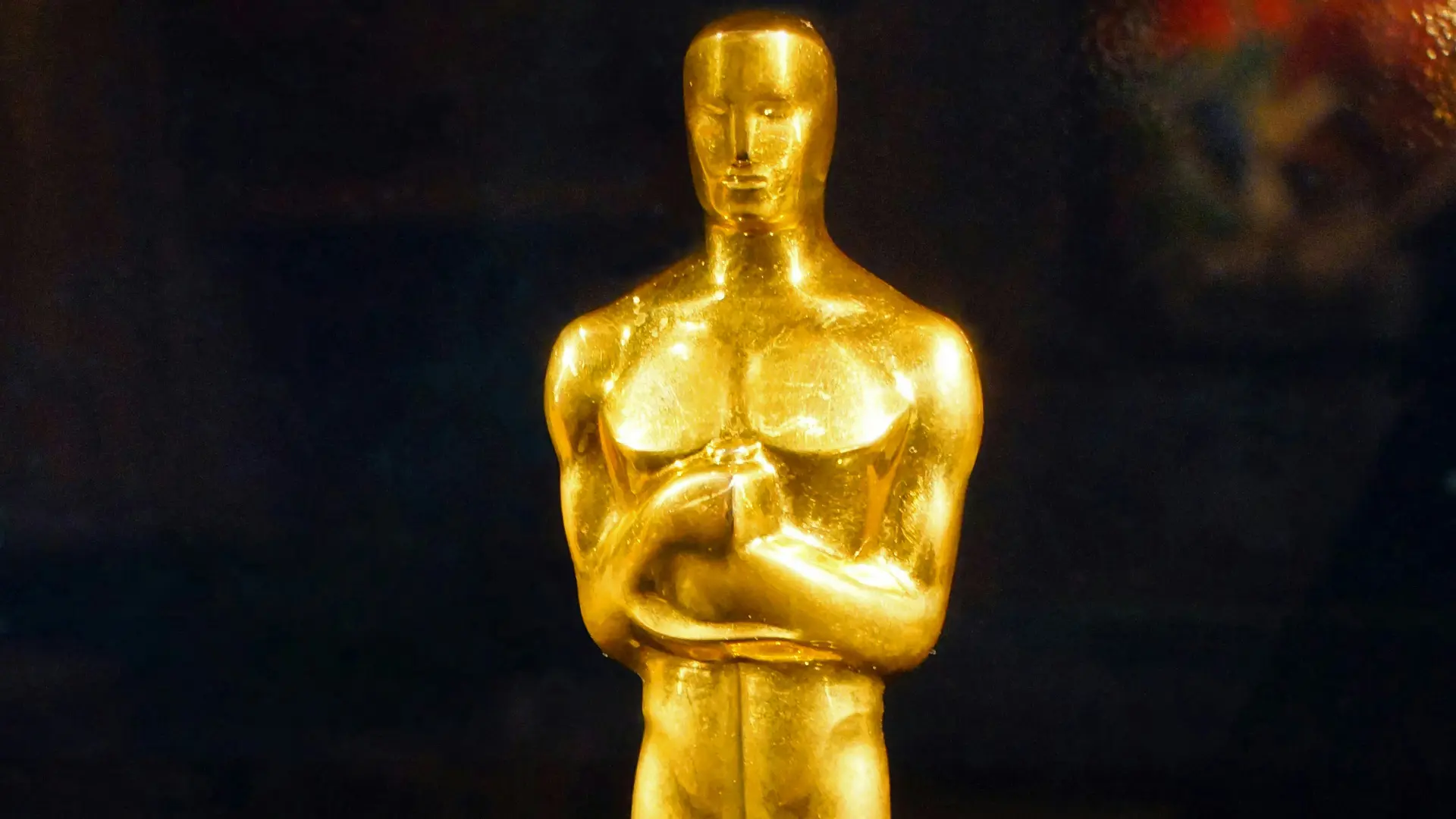 A photo of an Oscar - the Academy Award statuette of a golden man with his arms folded across his body against a black background.