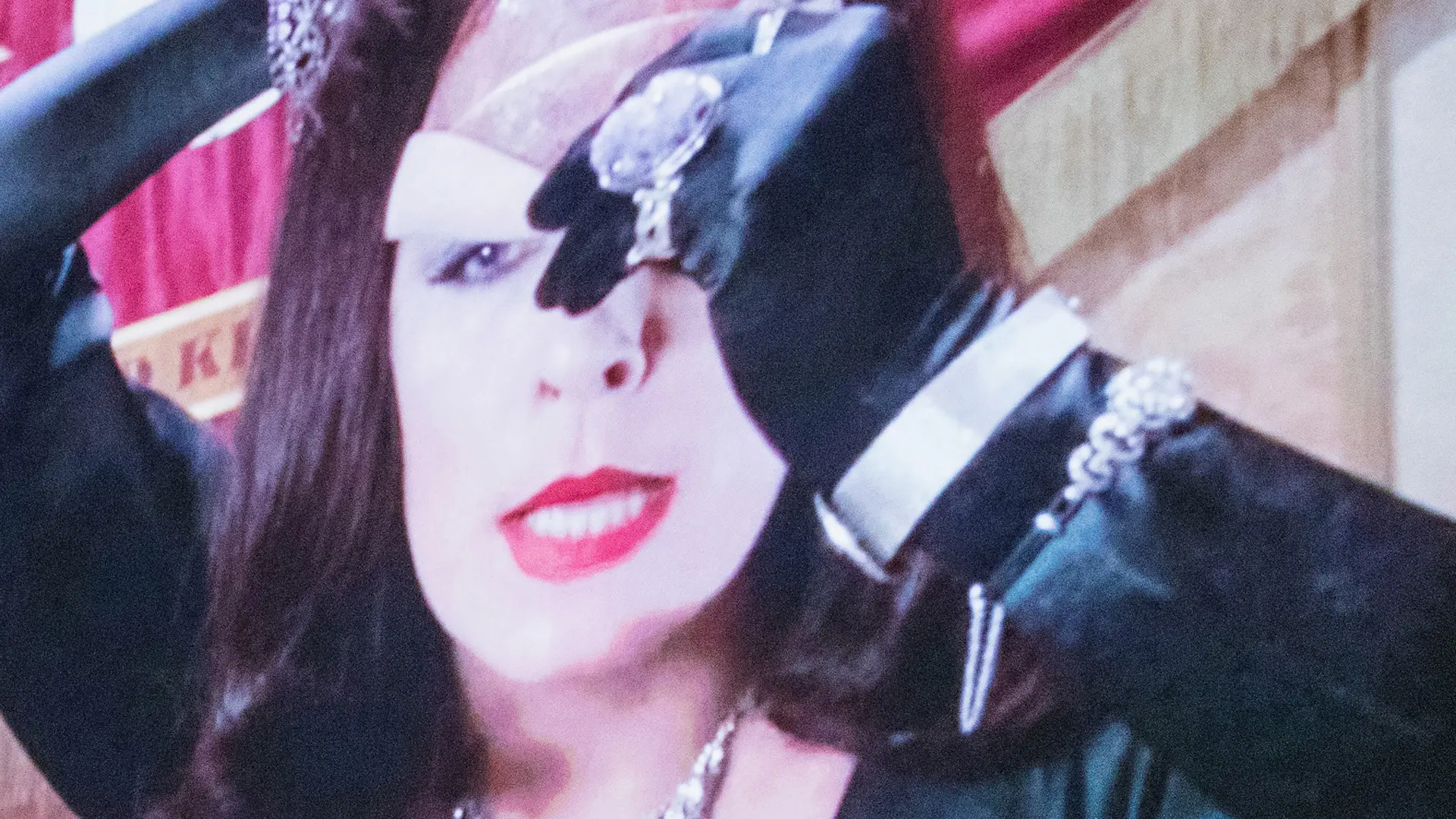 A still from the movie The Witches showing Anjelica Houston peeling off her mask with a black gloved hand.
