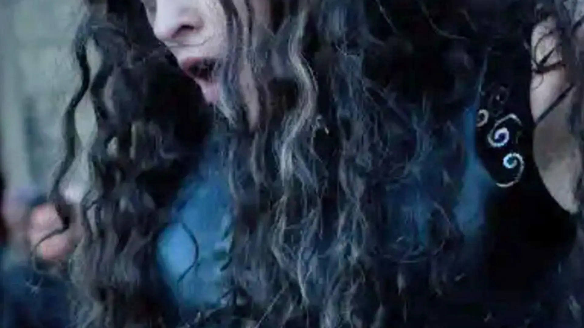 A close up of a dark curly haired woman with her mouth open wearing a black dress.