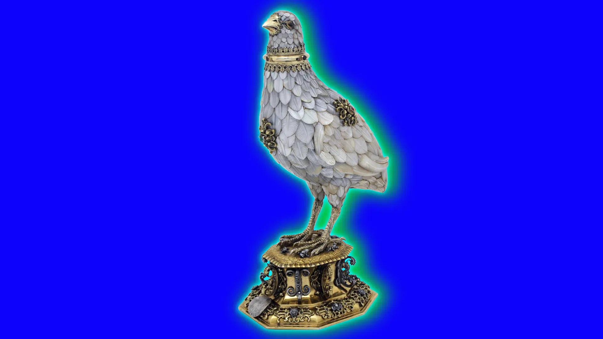 An image of a partridge statue made from shell, silver, gold and it is stood on a gold base, set against a royal blue background with a green halo.