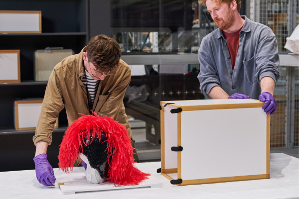 A V&A technician supports a visitor as they unbox a fringed stagewear headpiece
