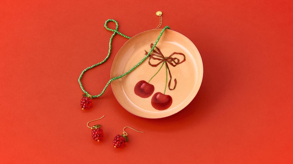 Lobster themed jewellery spills from a beaded clutch bag (also featuring a lobster) while a trinket tray featuring cherries is scattered with raspberry themed accessories