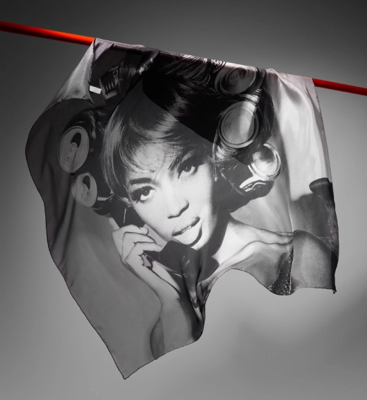 A silk scarf is caught in motion cascading over a red frame, with a spotlight on its feature - Naomi Campbell