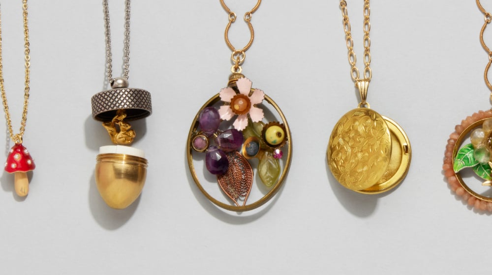 A row of whimsical necklaces featuring; a miniature mushroom, a squirrel inside an acorn-shaped locket, an abstract floral painted with beads, a classic Victorian locket, a second framed floral beadwork, a silver woodland scene, and a miniature book.