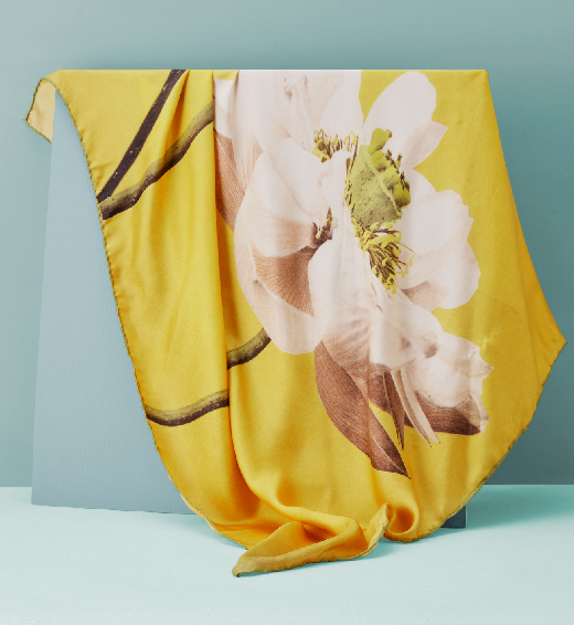 a bright yellow silk scarf with a large-scale photograph of a lotus flower is displayed on a board before a sky-blue background