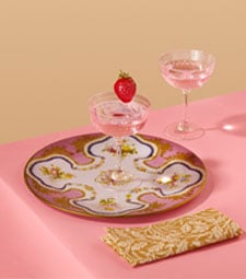 Drinkware and tableware inspired by the V&A Marie Antoinette Style exhibition. Crystal coupe glasses and a plate inspired by Sevres porcelain adorn a pastel pink tabletop.